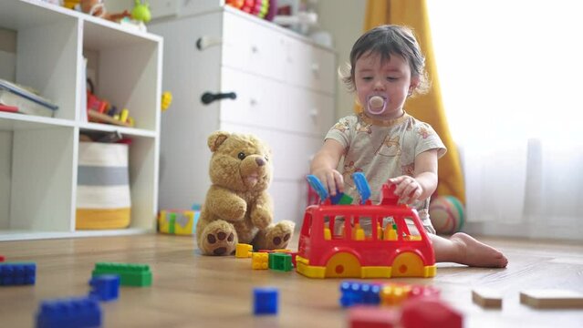 baby plays with toy bear a toy bus and puts wooden sticks in the hatch. development of fine motor skills concept. baby learns to put sticks toys into dream a bus car indoors in kindergarten