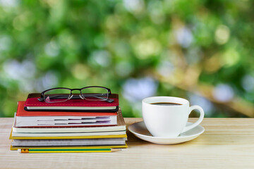 Coffee cup, glasses, and stack of book on wooden table with blur background