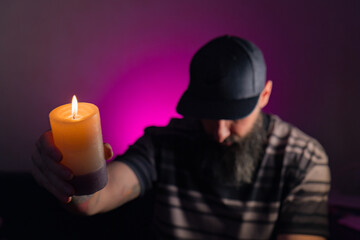 Bearded man holding a lit candle in his hand. Pink background