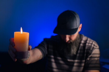 Bearded man holding a lit candle in his hand. Blue background