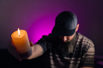 Bearded man holding a lit candle in his hand. Pink background