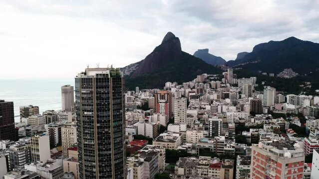 Aerial Downward Shot Of Tall Residential Building In City By Mountains By Wavy Sea Under Cloudy Sky - Rio de Janeiro, Brazil