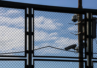 Surveillance cameras over barbed wire against a blue sky. Fenced guarded territory, no access. Area...