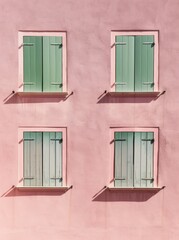 Fototapeta na wymiar A pink building with four windows featuring vibrant green shutters
