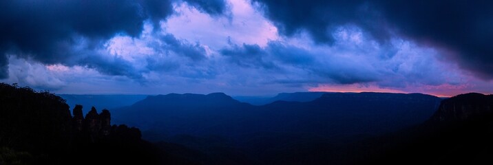 Three sisters rocky outcrops at nightfall with dark clouds and blue mountains
