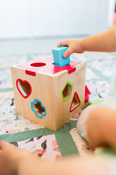 Toddler posting coloured shapes into wooden shape sorter box