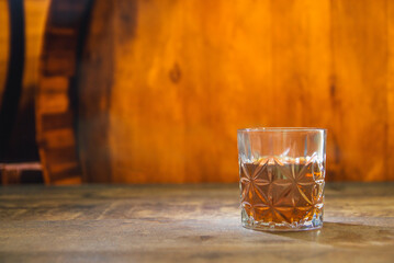 A glass of strong alcohol in a dark, dusty basement with oak barrels on an old texture table. Place...