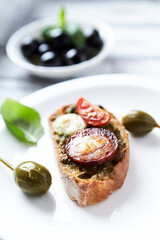 Crostini with tomato, salami and olive pesto on wooden background.