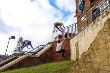 A group of men enjoying doing parkour in the city, each of them making a move, the blue sky is seen with clouds in the background