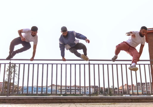 Three men jumping a fence at once, with the city and the sky in the background, front view. Concept of parkour