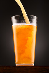 a glass of beer on a wooden stand and a dark black background, pouring beer into a glass, a close view of the object, the beer foams up and bubbles