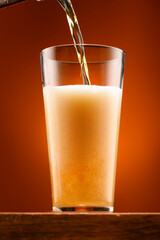 a glass of beer on a wooden stand and a light brown background, pouring beer into a glass, a close view of the object, the beer foams up and bubbles