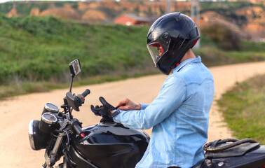 Young man putting on gloves on top of motorbike with le helmet on and road with landscape in background, casual dress