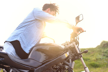 Curly haired Caucasian young man carrying his motorbike outdoors in direct sunlight. Lifestyle...