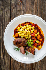 Baked pork cheeks with gnocchi and boiled vegetables in sauce on wooden table
