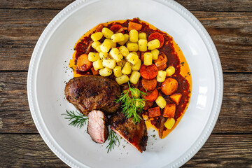 Baked pork cheeks with gnocchi and boiled vegetables in sauce on wooden table
