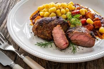 Baked pork cheeks with gnocchi and boiled vegetables in sauce on wooden table
