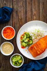 Seared salmon steak with boiled white rice and sliced cucumber on wooden table
- 765573735