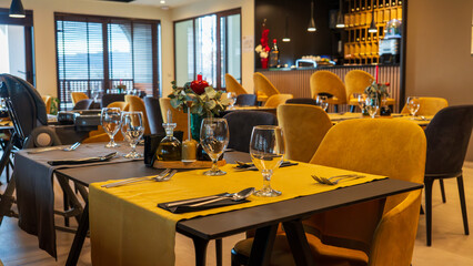 Restaurant scene with yellow tablecloths, glassware, and cutlery.