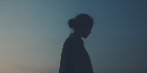 Silhouetted young woman in contemplation during twilight, her figure outlined by the fading light