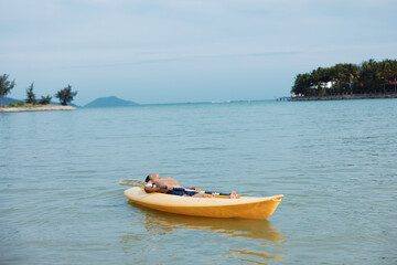 Fototapeta na wymiar Active Asian Man Enjoying Kayaking Adventure on a Tropical Beach