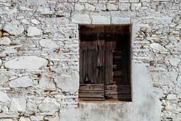 Fototapeta na wymiar Ventana rústica de madera en una pared de piedra encalada en Sanlúcar de Guadiana, España. Ventana rota de una casa antigua y deshabitada.
