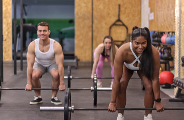 Fototapeta premium Group of multiracial smiling people doing deadlift with some bars with discs in a gym, front view. Fitness concept