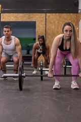 Group of multiracial people doing deadlift with some bars with discs in a gym, front view. Fitness concept