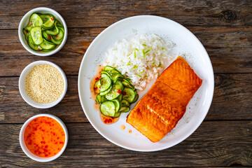 Seared salmon steak with boiled white rice and sliced cucumber on wooden table
- 765586360