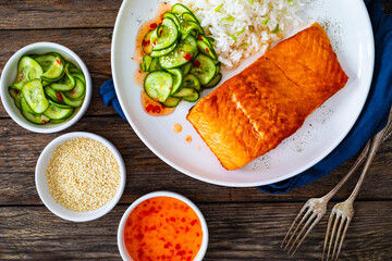 Seared salmon steak with boiled white rice and sliced cucumber on wooden table
- 765586512