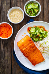 Seared salmon steak with boiled white rice and sliced cucumber on wooden table
- 765586577