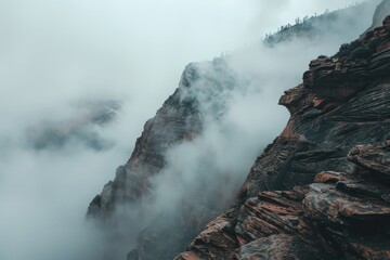 A rocky cliff engulfed in fog with low hanging clouds creating a mysterious atmosphere