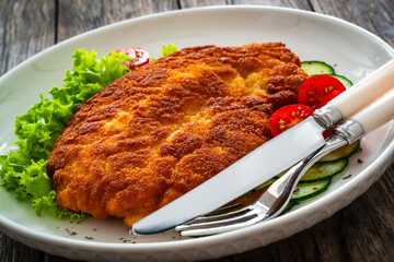 Crispy breaded fried pork chop and fresh vegetables on wooden table
- 765589332