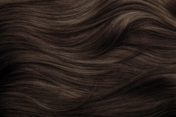Brown hair close-up as a background. Women's long brown hair. Beautifully styled wavy shiny curls....