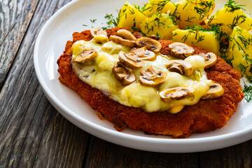 Crispy breaded seared pork chop with fried white mushrooms, cheese and boiled potatoes on wooden table
- 765590125