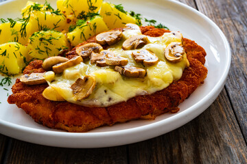 Crispy breaded seared pork chop with fried white mushrooms, cheese and boiled potatoes on wooden table
- 765590146
