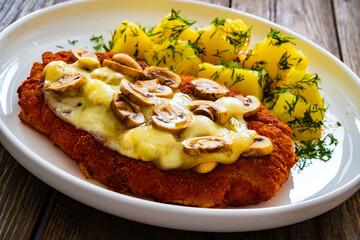 Crispy breaded seared pork chop with fried white mushrooms, cheese and boiled potatoes on wooden table
- 765590515