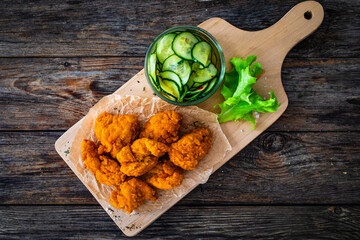 Fried breaded chicken nuggets served with fresh vegetables on wooden table
- 765591312
