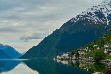 beautiful tranquil landscape at the beach of Hardanger fjord with calm green water and snow covered...