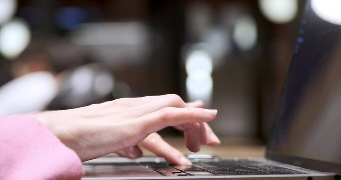This close-up shot depicts the hands of a young woman working with a computer in a café. As she types on the keyboard, her hands move swiftly and confidently