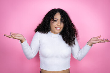 African american woman wearing casual sweater over pink background clueless and confused expression with arms and hands raised - obrazy, fototapety, plakaty