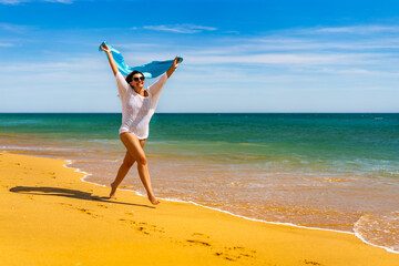 Beautiful woman walking on sunny beach holding shawl
- 765605312