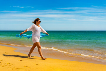Beautiful woman walking on sunny beach holding shawl
- 765605386