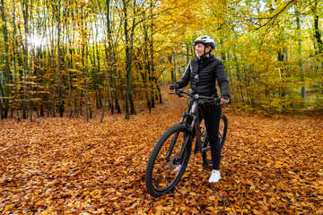 Fototapeta na wymiar Woman riding bicycle in city forest in autumn scenery 