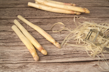 unpeeled and peeled white asparagus on a table. the asparagus peeler lies on the asparagus peelings