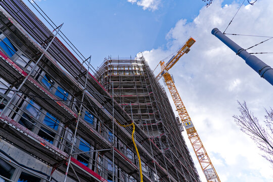 Looking up construction site of concrete apartment tower with yellow crane and scaffolding on a sunny spring day. Photo taken March 21st, 2024, Zurich, Switzerland.