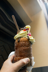Hand holding czech bakery  delicacy called trdelník  with chocolate, strawberries and cream topping.