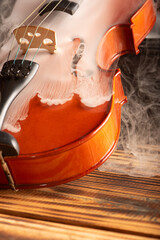 Obraz premium Violin with smoke, beautiful violin covered with a thin smoke screen on rustic wood and black background, selective focus.