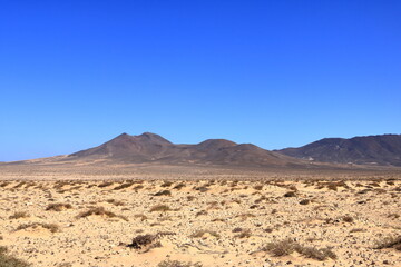 Gravel, dusty road with high volcanic mountains in the background. Jandia, Morro Jable, Fuerteventura, Canary Islands, Spain