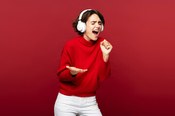 Woman with headphones on, listening music, gesticulating and pretending singing into microphone